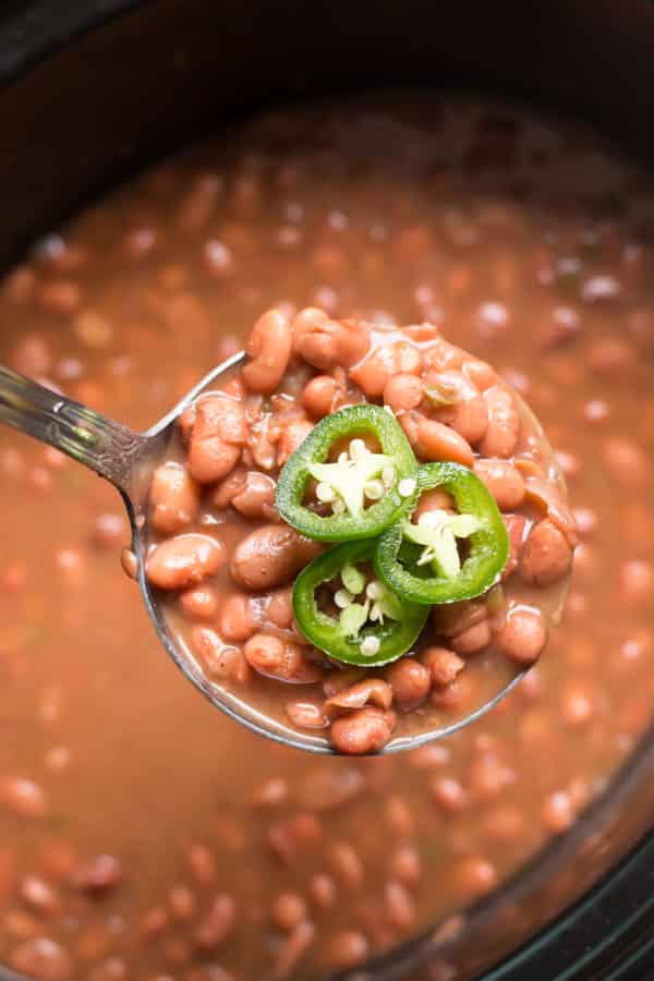 Pinto beans on a ladle coming from a slow cooker.