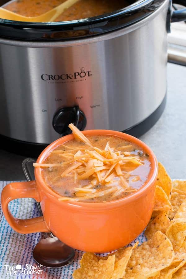 Orange bowl of enchilada soup with cheese on top.