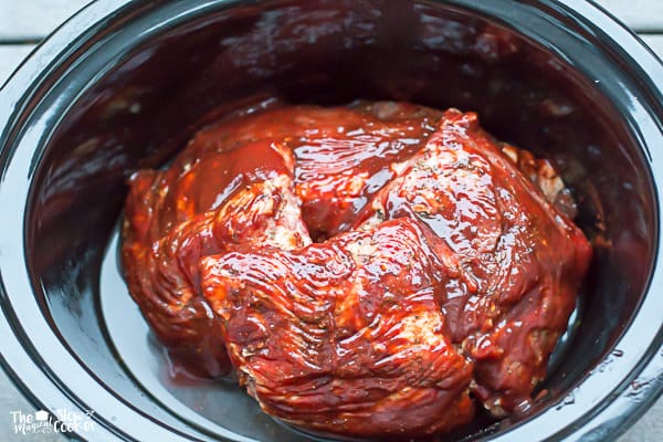 raw ribs in slow cooker slathered in barbecue sauce