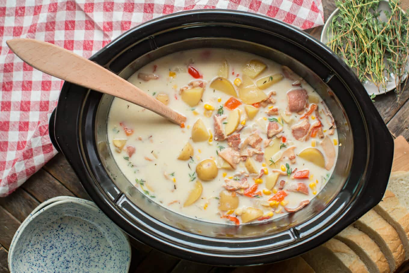 corn chowder in a slow cooker with wooden spoon in it.