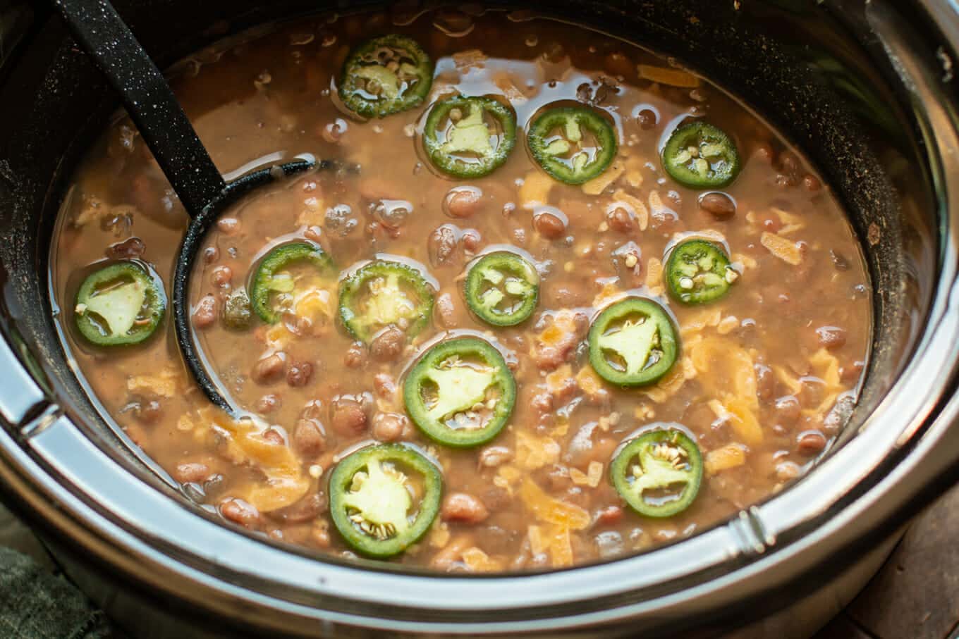 Close up of pinto beans with ladle and jalapenos on top.