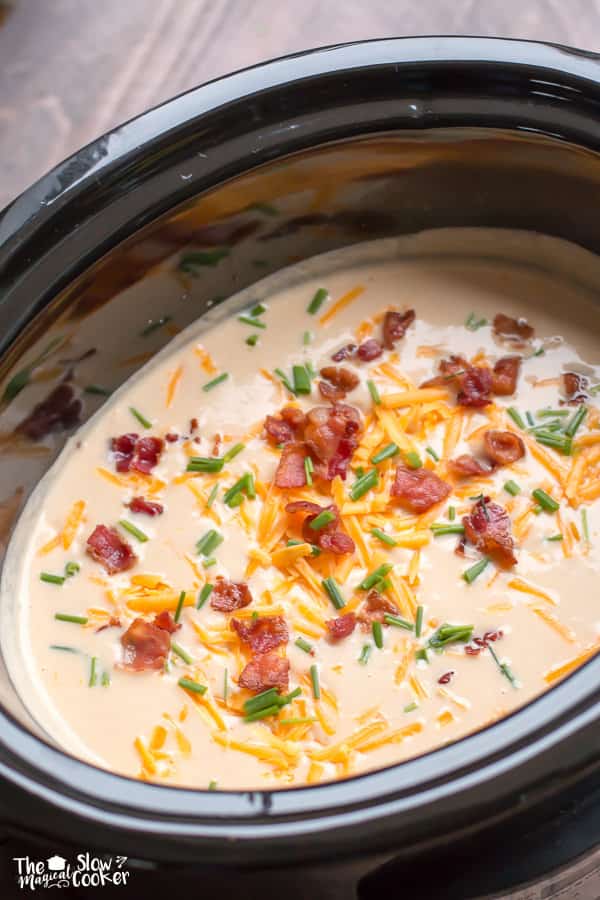 slow cooker with creamy cauliflower soup in it. Cheese, bacon, chives on top.