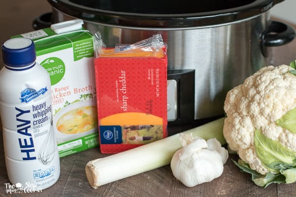 Chicken broth, heavy cream, leeks, sharp cheese, cauliflower and garlic in front of slow cooker.
