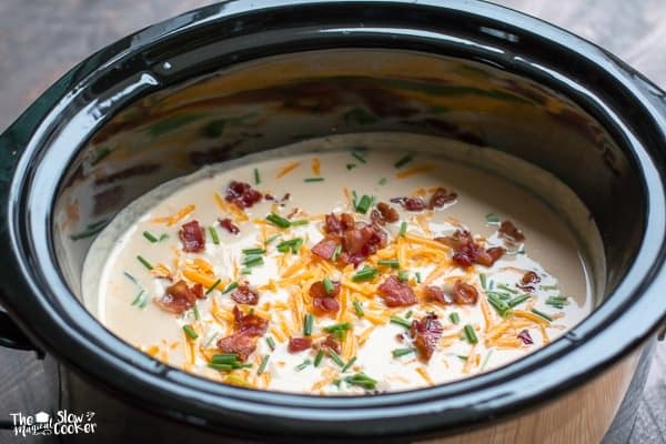 Close up of creamy cauliflower soup with cheese, bacon and chives on top.