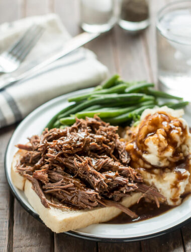 roast beef on white bread with mashed potatoes and green beans on a plate.