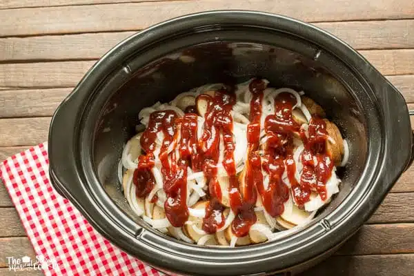 Patatas, cebollas y salsa barbacoa encima de las chuletas de cerdo en slow cooker.