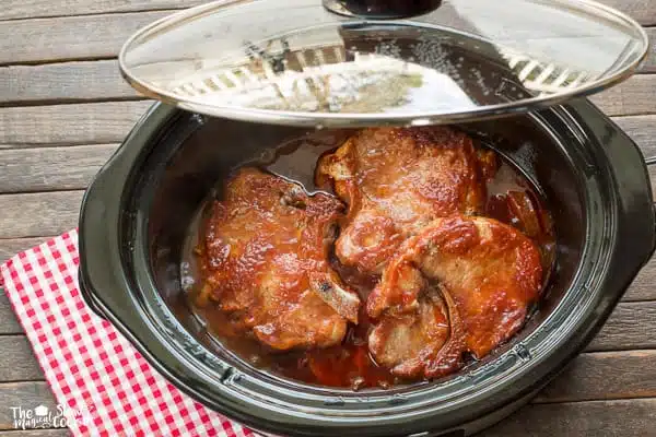 chuletas de cerdo a la barbacoa cocidas sobre patatas y cebollas en la olla de cocción lenta.