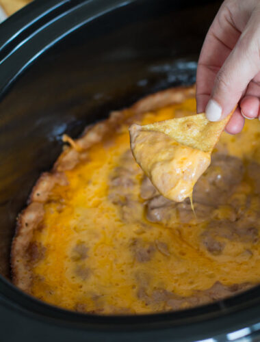 Creamy bean dip on chip in front of slow cooker.