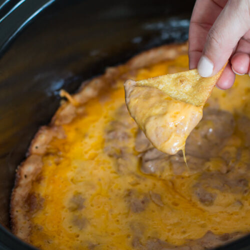 Creamy bean dip on chip in front of slow cooker.