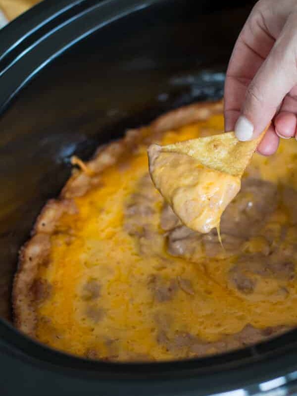 Creamy bean dip on chip in front of slow cooker.