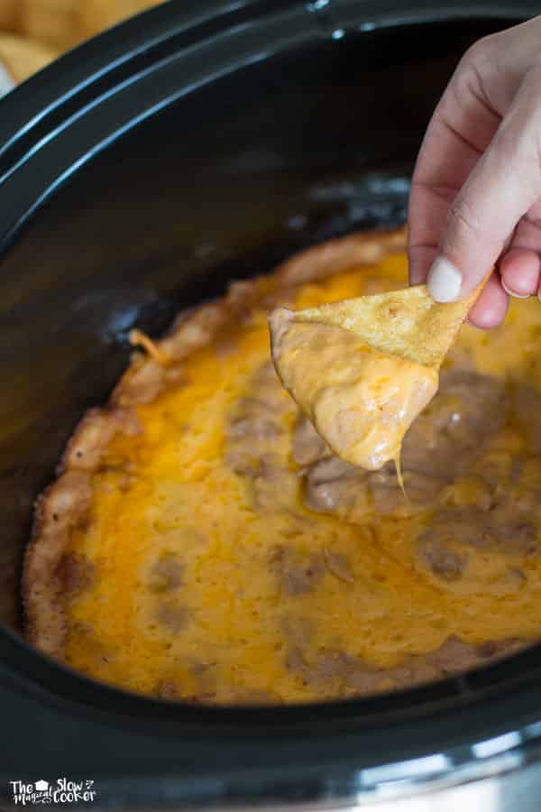 Creamy bean dip on chip in front of slow cooker.