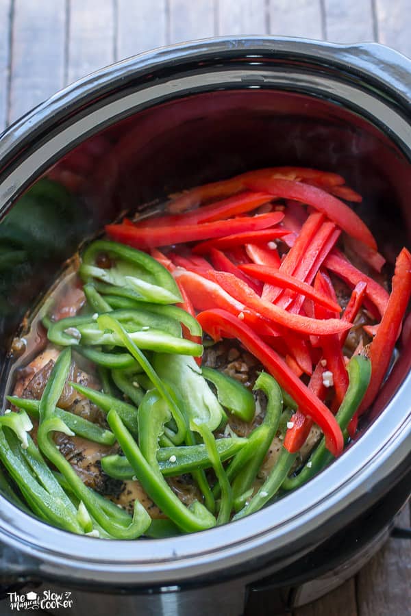 Cooked chicken in slow cooker with red and green bell peppers on top.