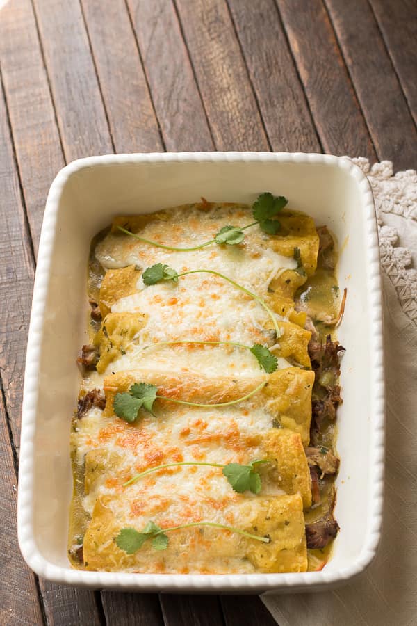 cooked pork enchiladas in white baking dish.