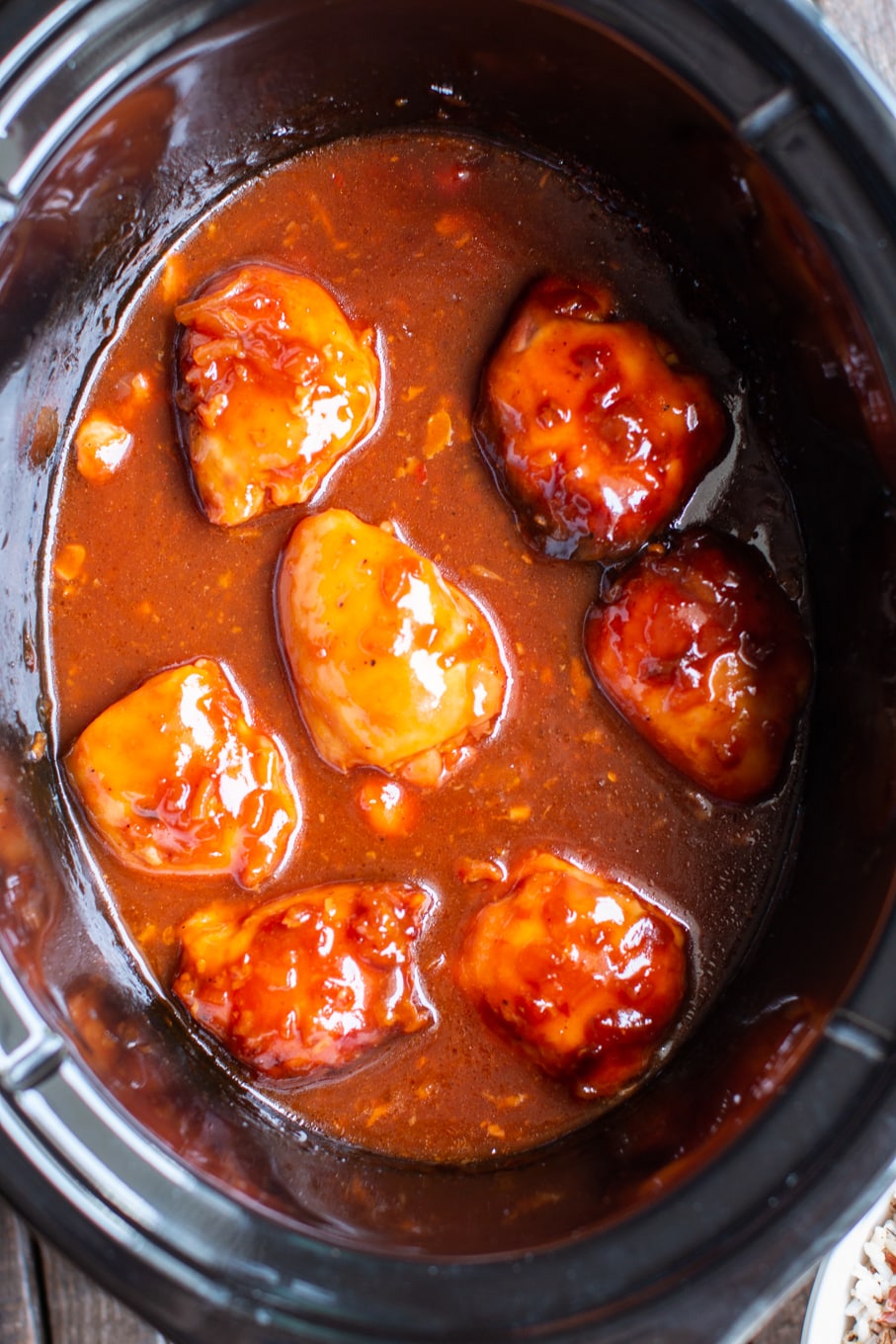 close up of chicken thighs in deep orange colored apricot sauce in slow cooker.