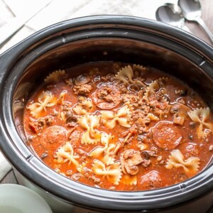 pizza soup in slow cooker with pepperoni and bowtie pasta in it.