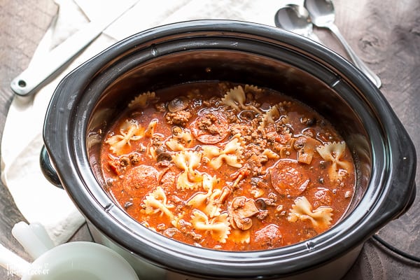 Slow cooker full of pizza soup with pepperoni and bow tie pasta