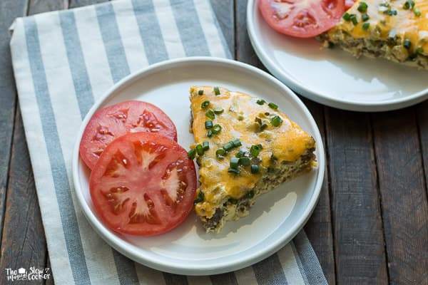 One piece of quiche with two slices of tomato on a white plate
