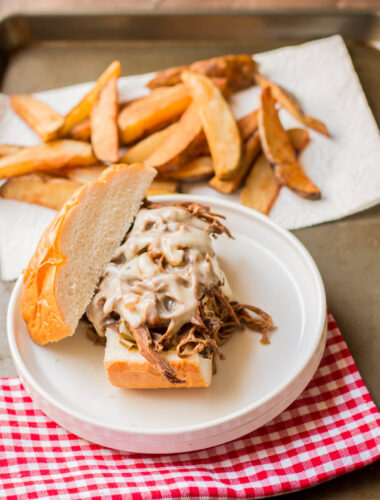philly cheese steak sandwich with wedge cut fries in background.