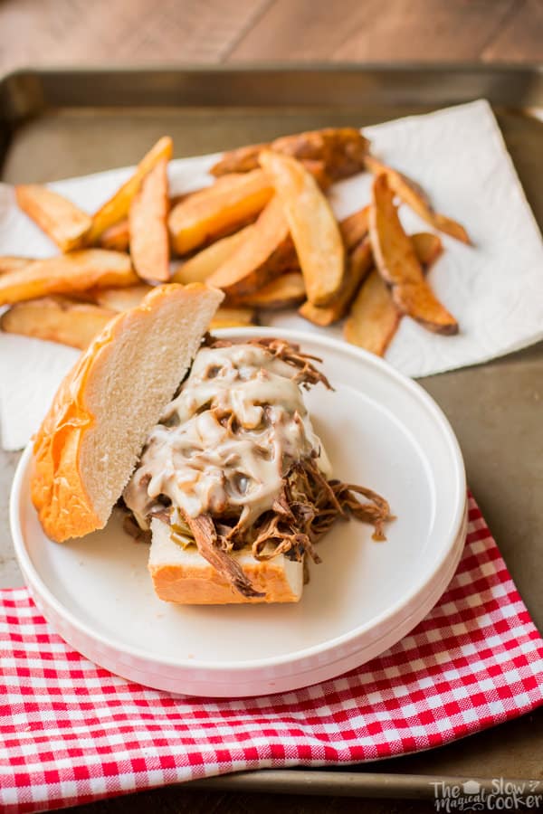 White plate with sandwich with shredded beef and swiss cheese on top.