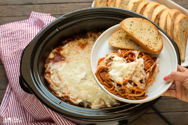 white plate of spaghetti with garlic bread on side, with slow cooker in background