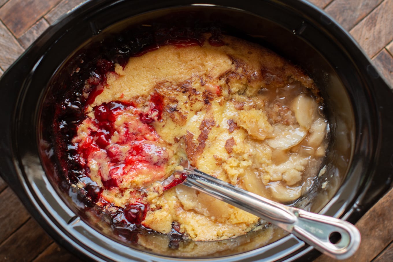 Spoon in cherry and apple cobbler in slow cooker.