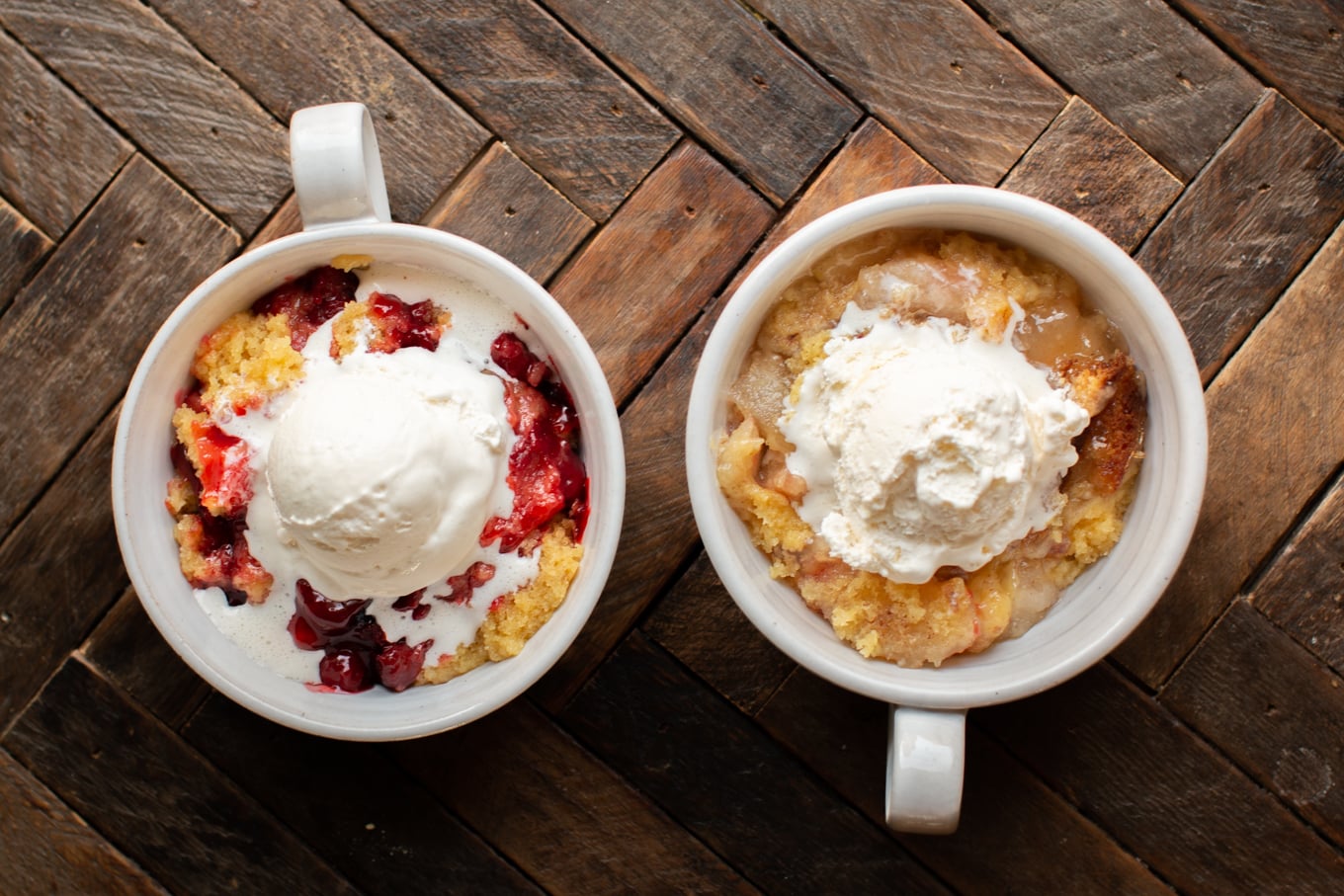 Bowl of cherry cobbler, bowl of apple cobbler both with ice cream on top.