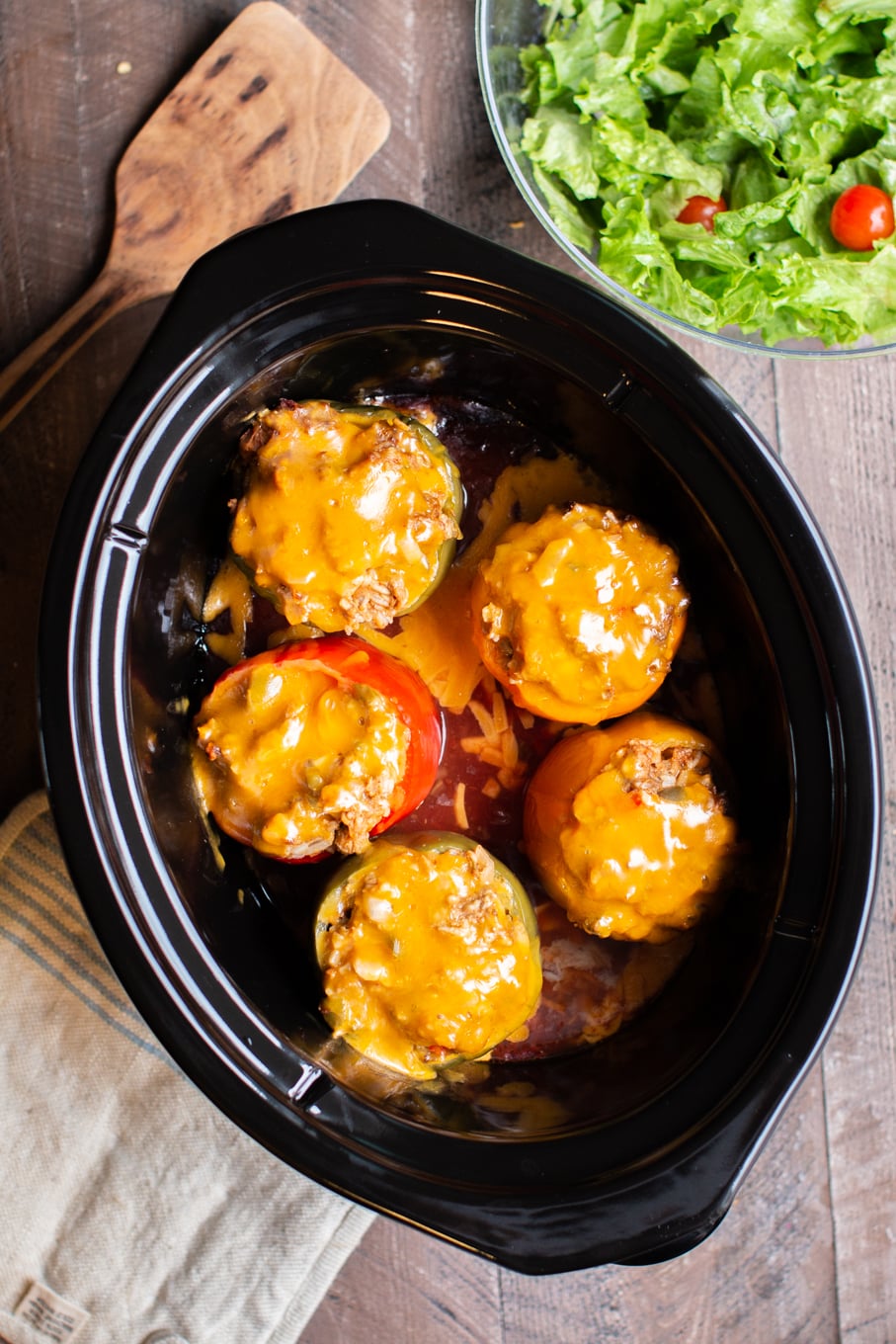 Five stuffed peppers in slow cooker with cheese on top.