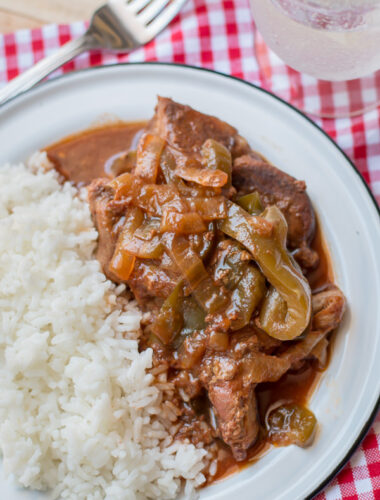 close up of ribs with bell peppers and onions on plate with white rice