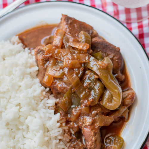 close up of ribs with bell peppers and onions on plate with white rice
