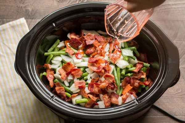 sweet potatoes, green beans and bacon in slow cooker with water being pour over