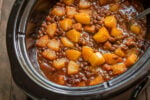 baked beans with chunks of pineapple on top in slow cooker.