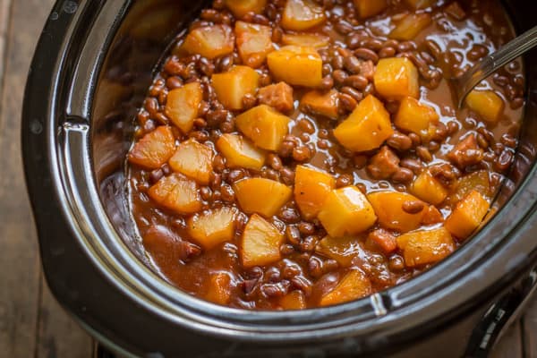baked beans in slow cooker with pineapple and a ladle inside of beans.