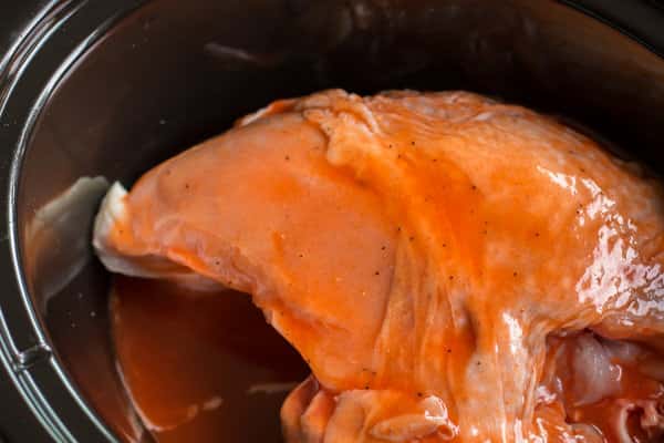 raw bone in turkey breast in slow cooker with honey, buffalo sauce and pepper on top.