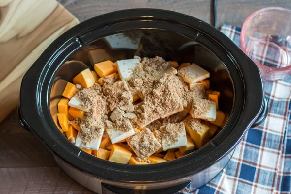 Cubed butternut squash with butter slices and brown sugar on top in the slow cooker.