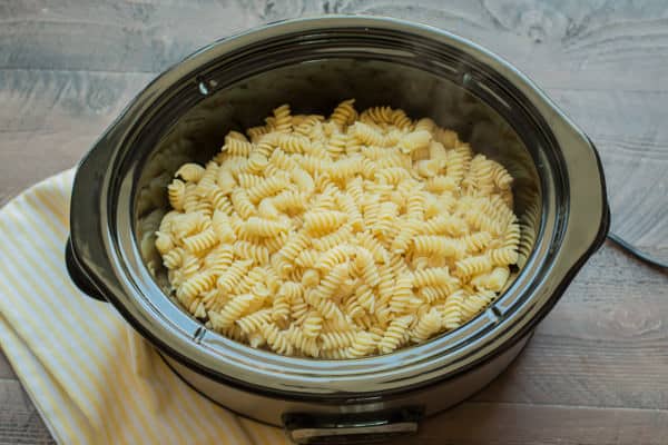 cooked rotini pasta on top of chicken in a slow cooker