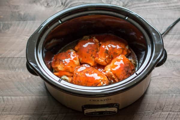 chicken thighs with buffalo sauce on top in the slow cooker, uncooked.