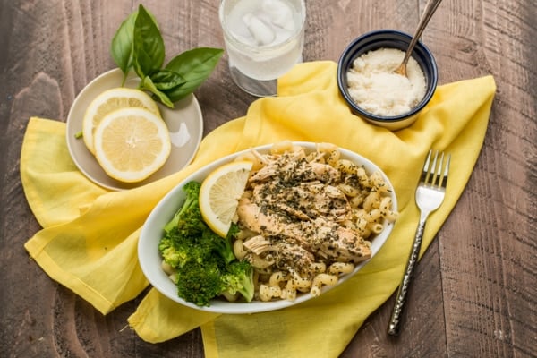 curly noodles, chicken, broccoli, and lemon in an oval bowl.