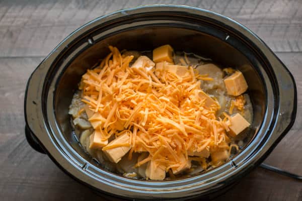 cheeses on top of cooked potatoes and broth in a slow cooker.