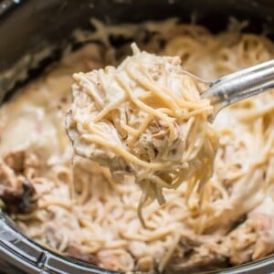 a scoop of chicken tetrazzini on a spoon coming from a slow cooker.