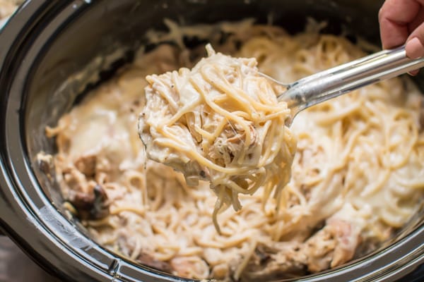 a scoop of chicken tetrazzini on a spoon coming from a slow cooker.