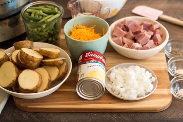 cream of chicken soup, ham, cheese, onion, potatoes and green beans on a cutting board.
