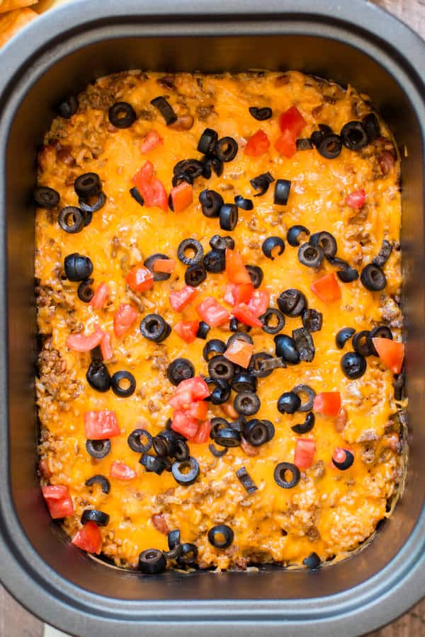 enchilada dip in a slow cooker with cheese, tomato and olives.