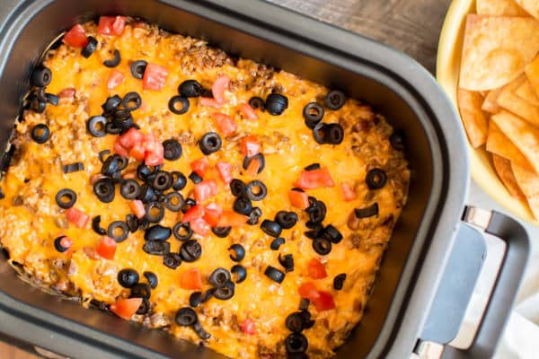 beef and enchilada dip in a slow cooker with chips on the side.