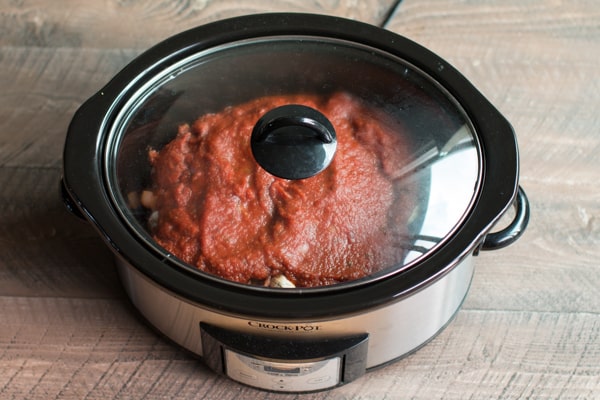 marinara sauce on top of chicken in a slow cooker.