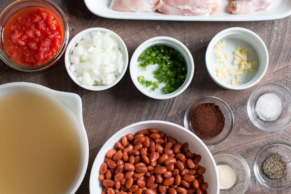 pinto beans, onoin, jalapeno, diced tomatoes, seasoniings, garlic and chicken thighs on a table.
