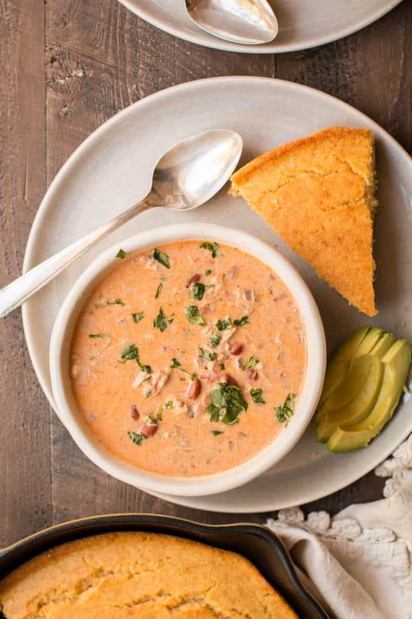 bowl of cream cheese chicken chili with cornbread and avocado on the side.