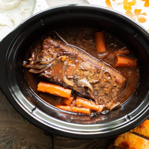 finished cooking brisket in the slow cooker with mashed potatoes and carrots on the side.
