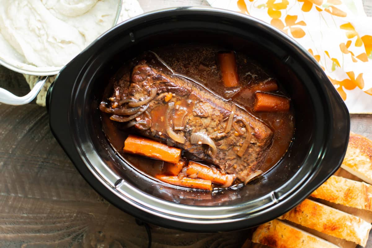 brisket in the slow cooker with mashed potatoes, carrots, and bread on the side.