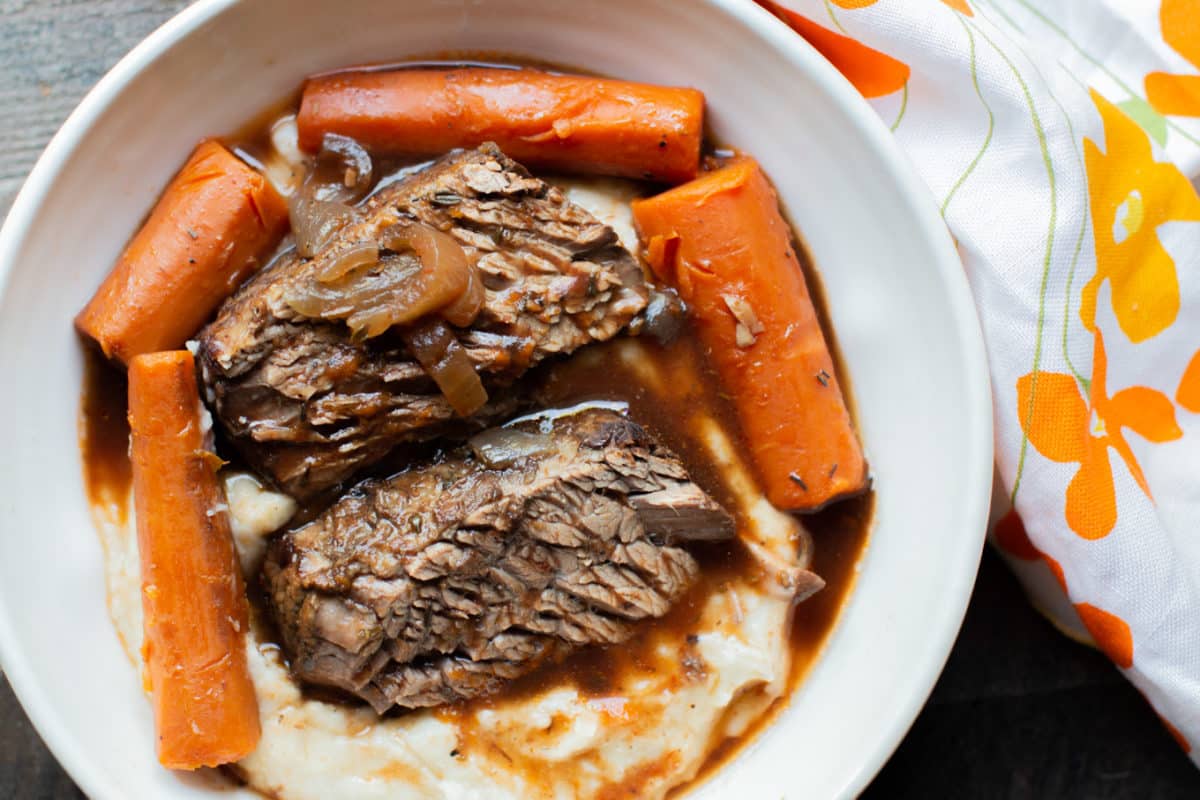 Bowl of mashed potatoes with sliced brisket and carrots and sauce.