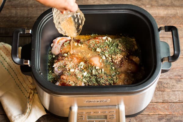 chicken thighs in a slow cooker with Italian dressing being poured over.